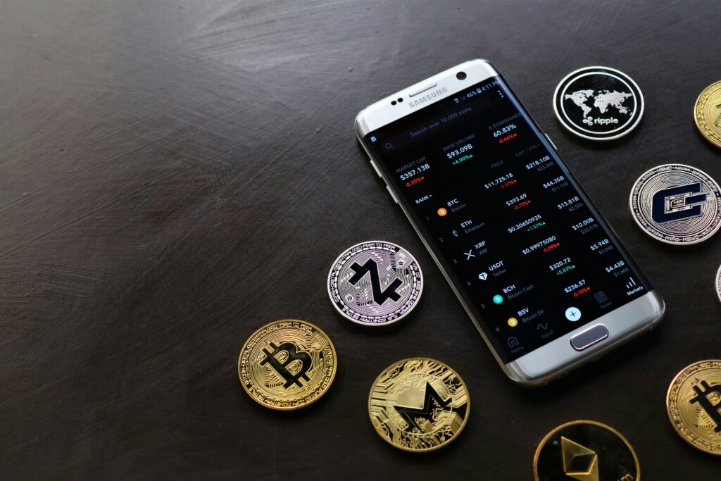 A collection of cryptocurrency coins and a smartphone displaying a digital trading platform.