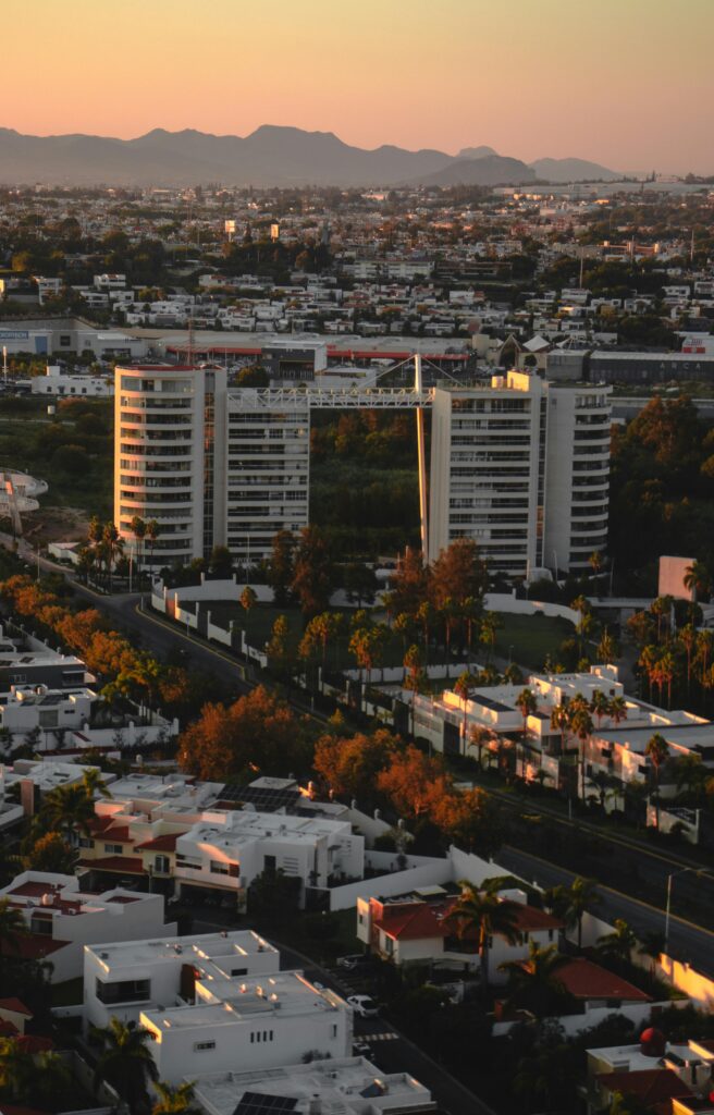 pexels-photo-18604178-18604178 Stunning aerial view of a cityscape at sunset with modern buildings and distant mountains.