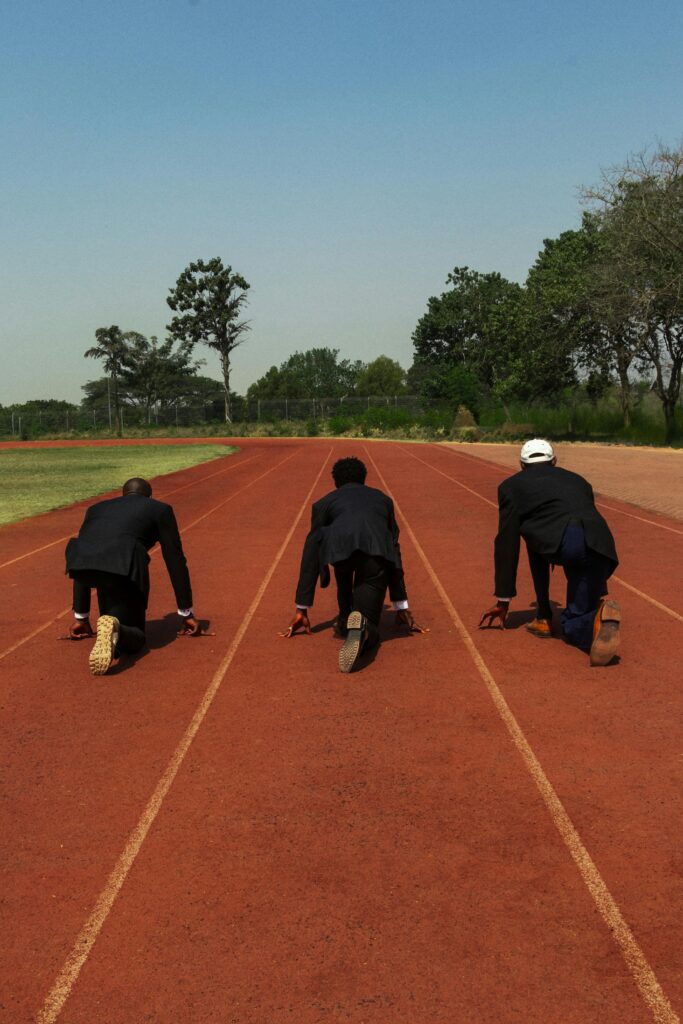 Three businessmen in suits crouched at the starting line on an outdoor running track.