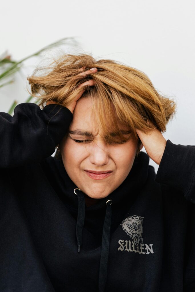 Young person expressing stress, holding head with closed eyes, symbolizing anxiety and frustration.