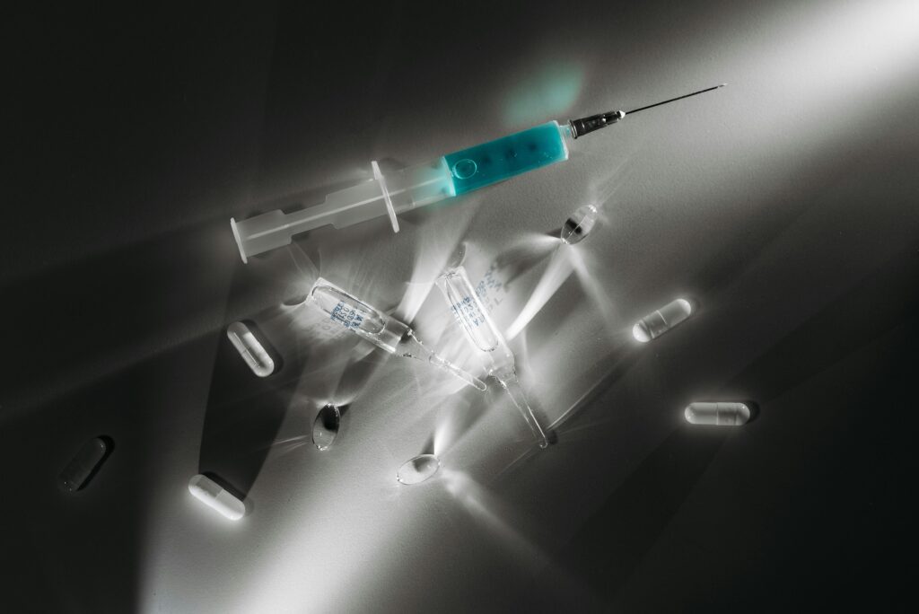 High contrast image of medical supplies, including a syringe and capsules, in a monochrome setting.