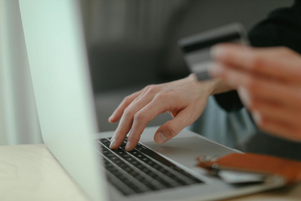pexels-photo-6633607-6633607 Close-up of hands holding a credit card and typing on a laptop keyboard for online shopping.