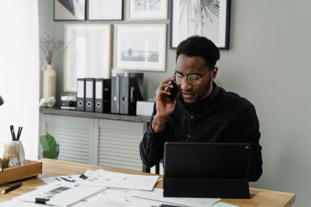 Professional man working at his desk on a call, managing documents and using a tablet.