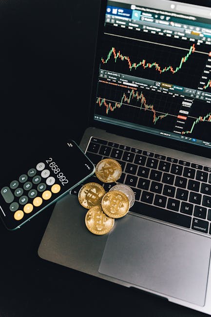 A still life of Bitcoin coins, a smartphone calculator, and a trading chart on a laptop.