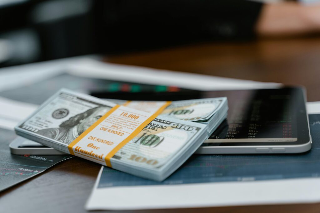 pexels-photo-7567304-7567304 A stack of $100 bills placed on a tablet displaying financial graphs, representing modern finance.