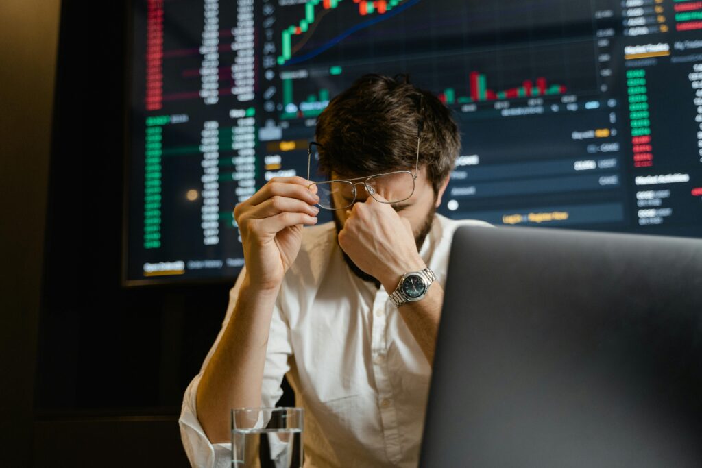 pexels-photo-7567537-7567537-1 A stressed man looks at stock market data on his computer screen in an office setting.