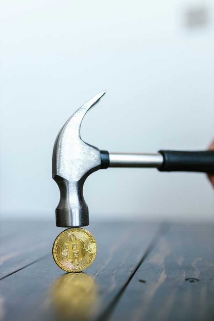 Close-up of a hammer striking a Bitcoin coin on a wooden surface, symbolizing cryptocurrency impact.