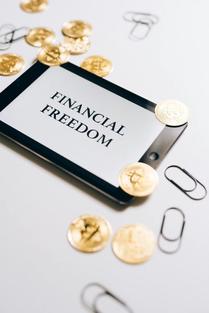 pexels-photo-8919505-8919505-1 Coins are scattered around a digital tablet displaying 'Financial Freedom', symbolizing cryptocurrency wealth.
